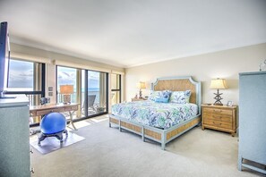 A spacious bedroom with a large bed, a desk, and a chair, featuring a view through a glass door. - Premier Oceanfront Top Floor Condo With Wraparound Balcony & Windows (Key Colony Beach)