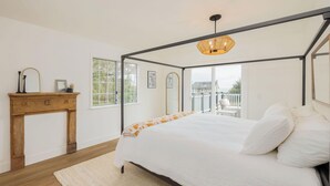 A bedroom with a four-poster bed, a wooden nightstand, and a large window with a view of the outside.