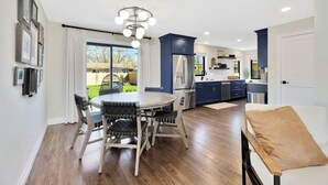A modern kitchen with a central island, dark blue cabinets, and a stainless steel refrigerator. - King Beds in Safe Area • Game Room • Patio & Grill (Wichita)