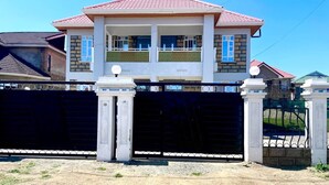 A two-story house with a red-tiled roof, a balcony, and a gated entrance.