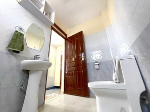 Ein Badezimmer mit einem weißen Waschbecken, einem Spiegel, einer Holztür und einer Toilette.