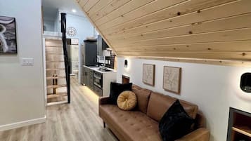 Una sala moderna con un sofá de cuero marrón, techo de madera y una cocina al fondo.