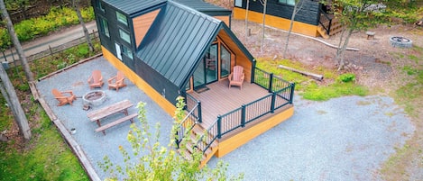 Una cabaña con terraza, mobiliario exterior y una chimenea.