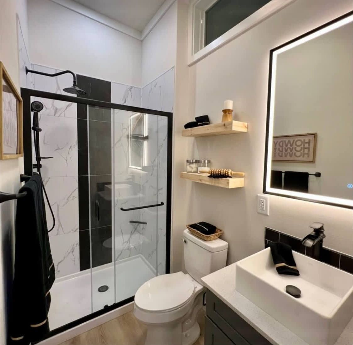A modern bathroom with a glass-enclosed shower, a white toilet, a sink with a mirror, and a towel rack.