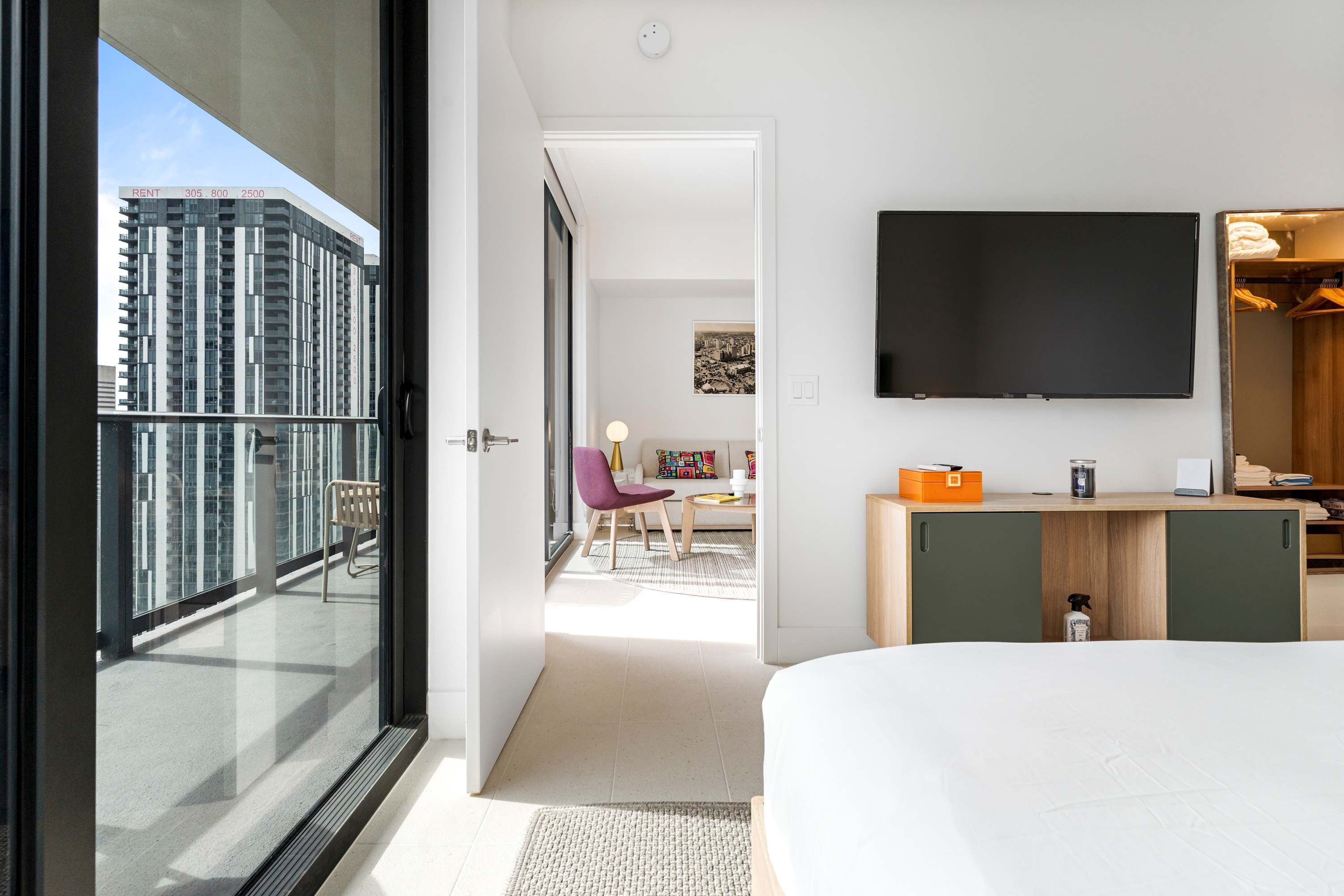 Quarto de hotel moderno com varanda, televisão na parede e escrivaninha com cadeira.