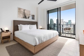 A modern bedroom with a large bed, a nightstand with a phone, and a view of a city skyline through a balcony. - Rumrunner Downtown Pool Gym Full Service Tower (Miami)