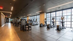 A gym with cardio machines, weight equipment, and large windows offering city views.