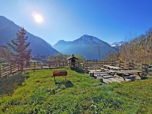 A rustic wooden fence, picnic tables, and a bench in a mountainous area with clear skies.