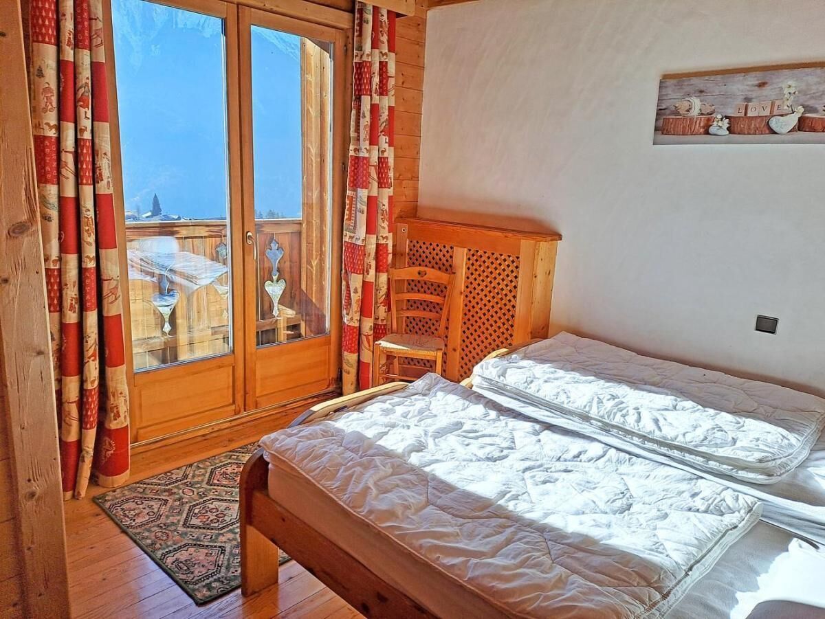 Une chambre avec deux lits, une chaise en bois, une petite table et une vue à travers une porte vitrée.