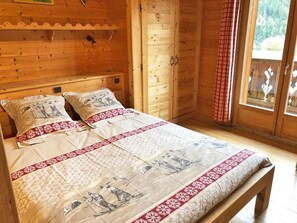 A wooden cabin bedroom with a bed, pillows, and a window with a view of trees. - Chalet, wifi, view mountain, sauna, balcony, fireplace or stove, 140m², Champagny-en-Vanoise (Champagny-en-Vanoise)