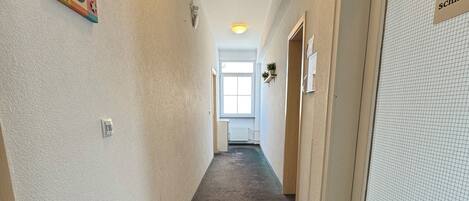 A hallway with a carpeted floor, a door with a sign, and a window at the end.