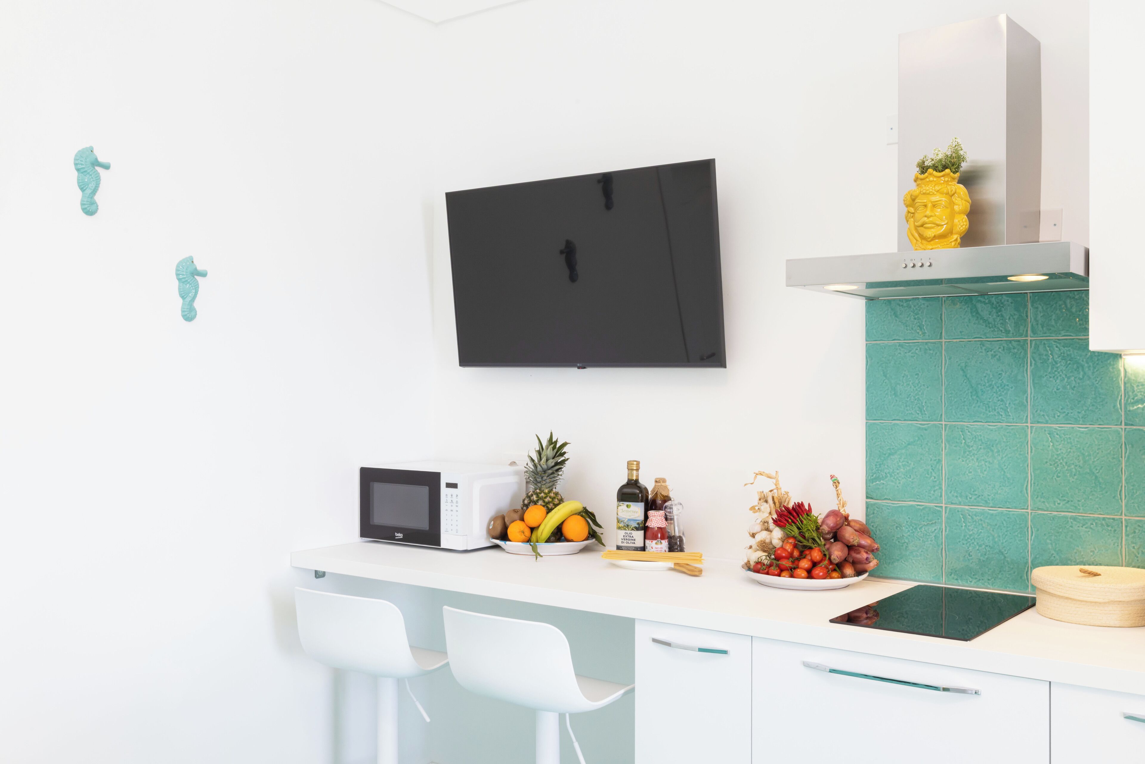 A modern kitchen with a flat-screen TV, a microwave, and a fruit bowl on the counter.
