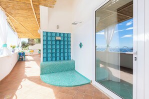 Un balcone con pavimento piastrellato, un'area salotto con motivo decorativo e una porta vetrata che dà su uno spazio esterno.