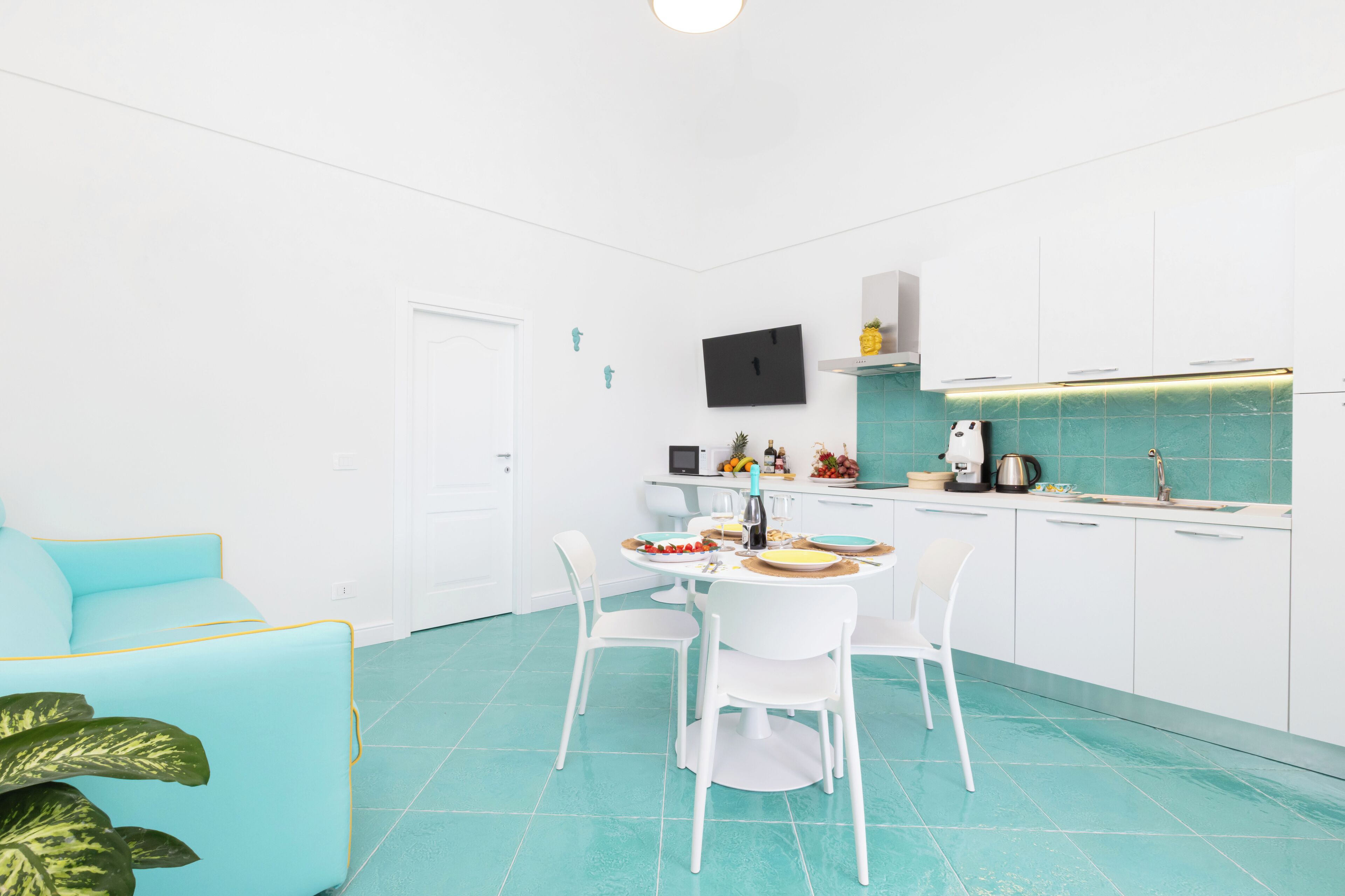 A modern kitchen with white cabinets, a dining table with chairs, and a teal floor.