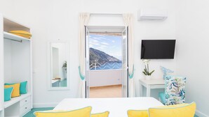 Una camera d'albergo con un letto, una televisione, un balcone vista montagne e una scrivania con una pianta.