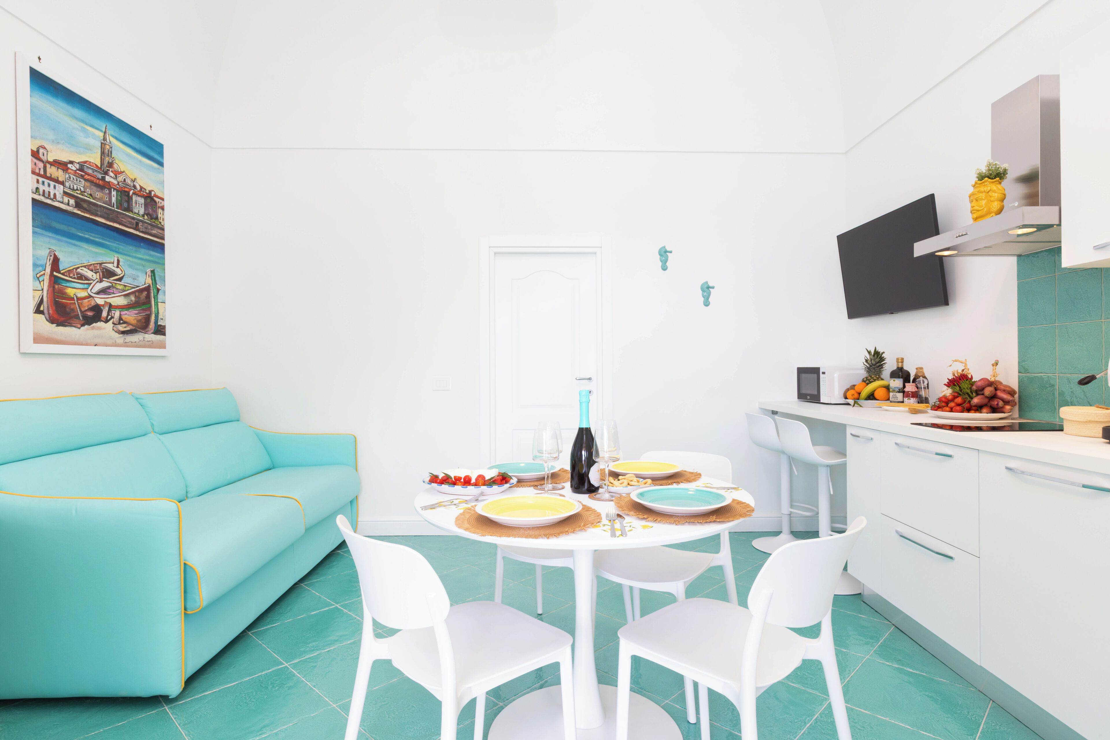 A modern kitchen with white cabinets, a teal countertop, and a dining area with a white table and chairs.