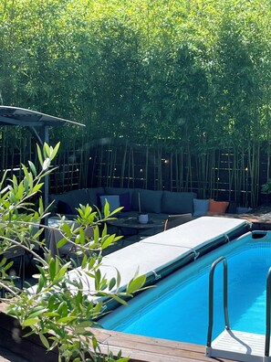 Un espace piscine avec un coin salon et des plantes en bambou.