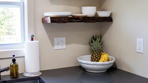 Una cocina con un lavamanos, encimera y repisas de madera con cuencos y platos.