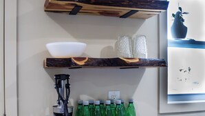 Una cocina con estantes de madera que sostienen utensilios de cocina, una tabla de cortar con limones y botellas verdes.