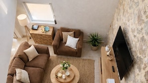 A loft-style living room with a stone wall, a large window, a sofa set, a coffee table, and a flat-screen TV. - Stone Villa with Fully Private Pool not overlooked & AC - 20 min from Beaches (bizanet)