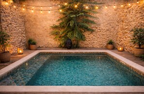 Una piscina rectangular con agua cristalina, rodeada de muros de piedra y plantas en macetas.