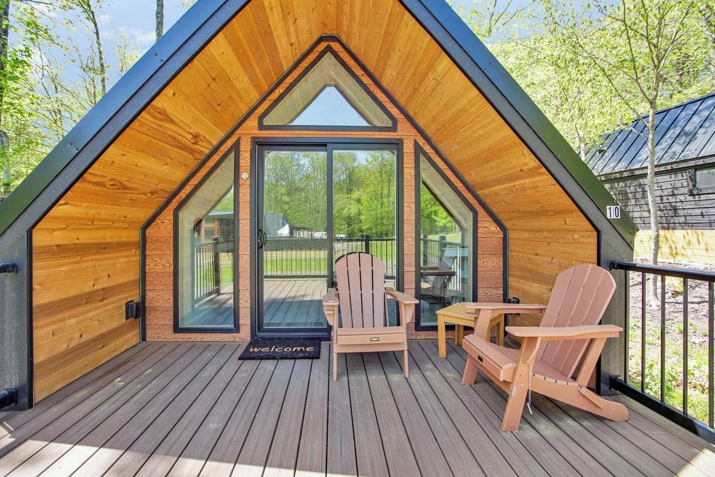 Una baita di legno con tetto spiovente, una veranda con due poltrone Adirondack e un ingresso con porta in vetro.