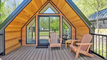 Una baita di legno con tetto spiovente, una veranda con due poltrone Adirondack e un ingresso con porta in vetro.