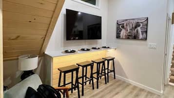 A compact kitchen with a TV, bar stools, and a high ceiling with wooden beams.