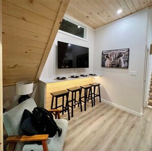 A compact kitchen with a TV, bar stools, and a high ceiling with wooden beams.