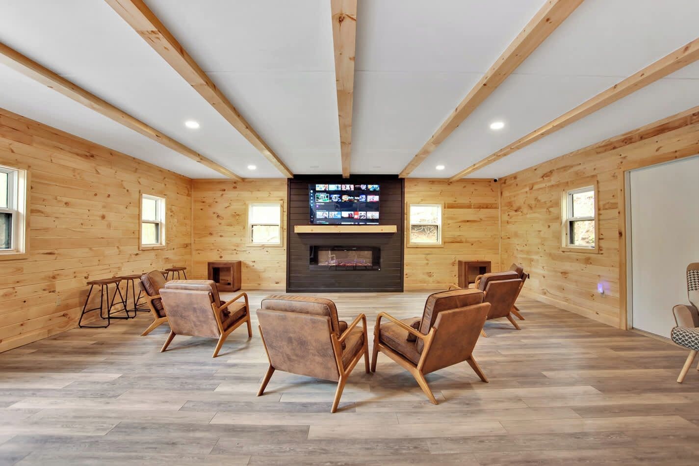 A spacious room with wooden walls, a large TV screen, and several leather chairs arranged around a central fireplace.