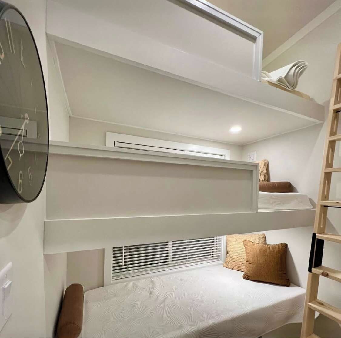 A compact room with a bunk bed, a wall clock, an air conditioning unit, and a window with blinds.