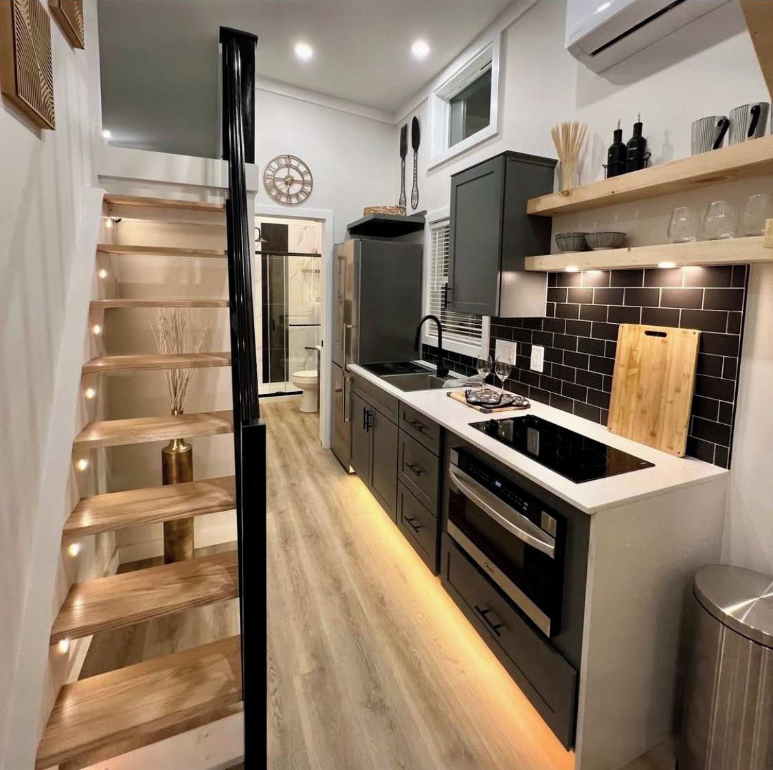 A modern kitchen with a central island, built-in appliances, and a wooden staircase.