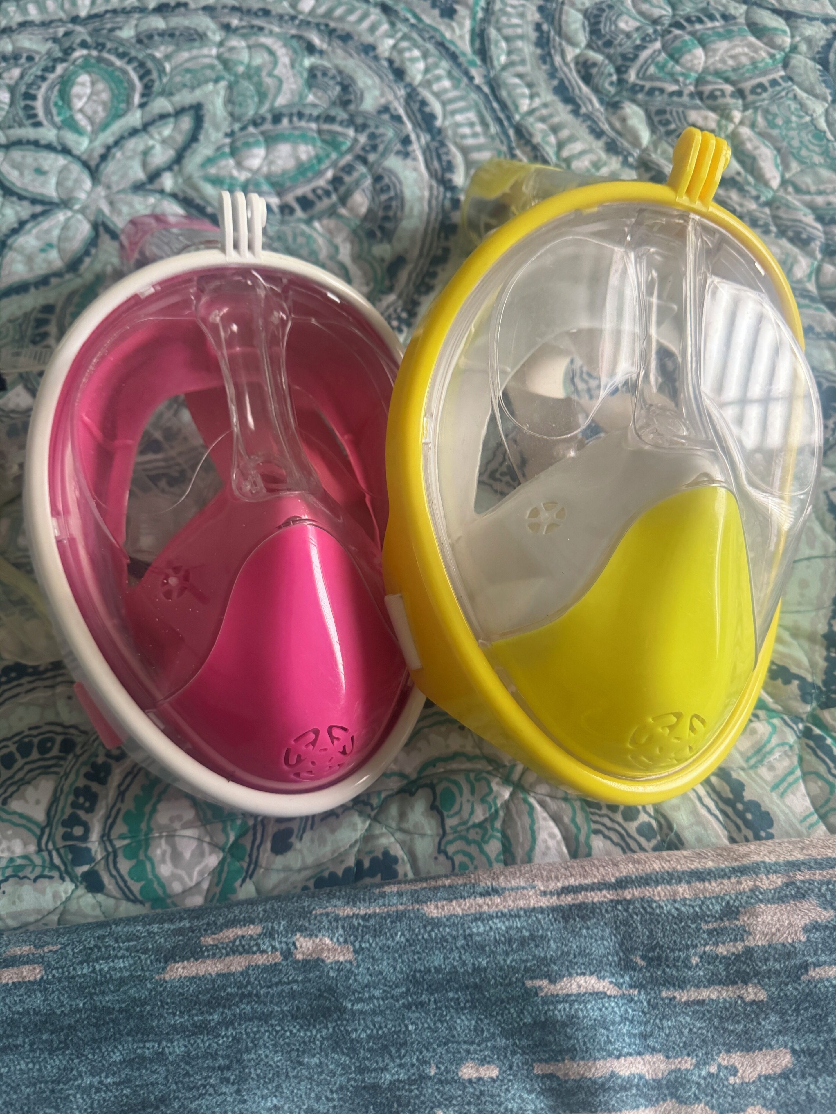 Two baby bottles, one pink and one yellow, on a patterned fabric surface.