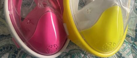 Two baby bottles, one pink and one yellow, on a patterned fabric surface.