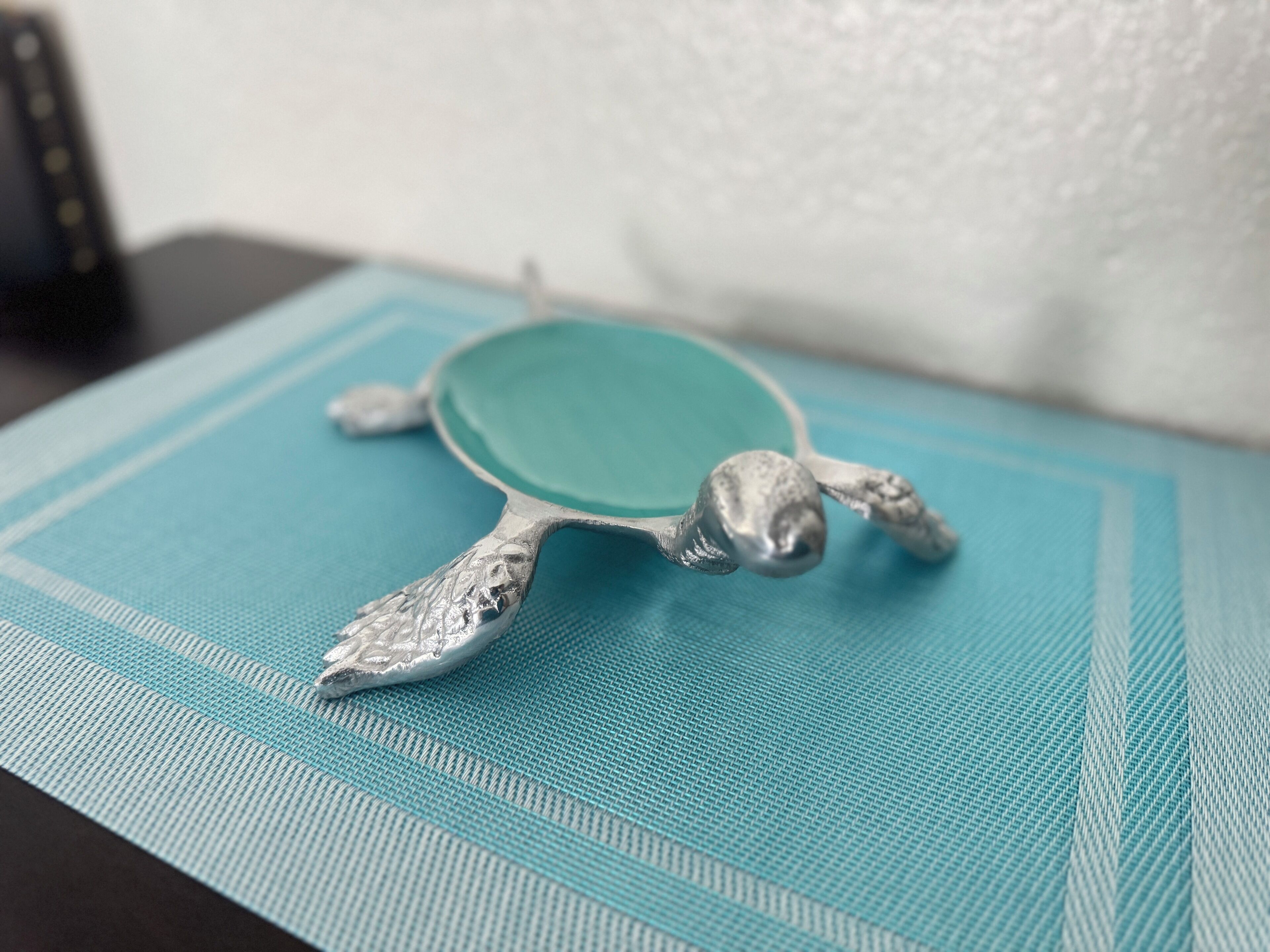 Un objet en forme de tortue, de couleur argentée, posé sur une surface bleue texturée.