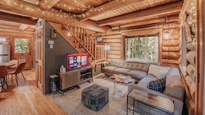 A cozy log cabin interior with a wooden staircase, a sofa, a television, and a dining area. - 81sl - Hot Tub - Wifi - Pets Ok - Sleeps 4 (Deming)