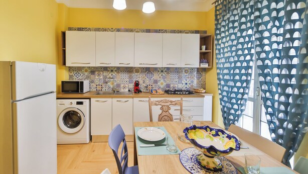 A compact kitchen with a washing machine, microwave, and a dining area with a table set for two. - AeP House (Pompei)