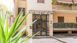 A building entrance with a glass door, a metal gate, and a balcony with plants. - AeP House (Pompei)