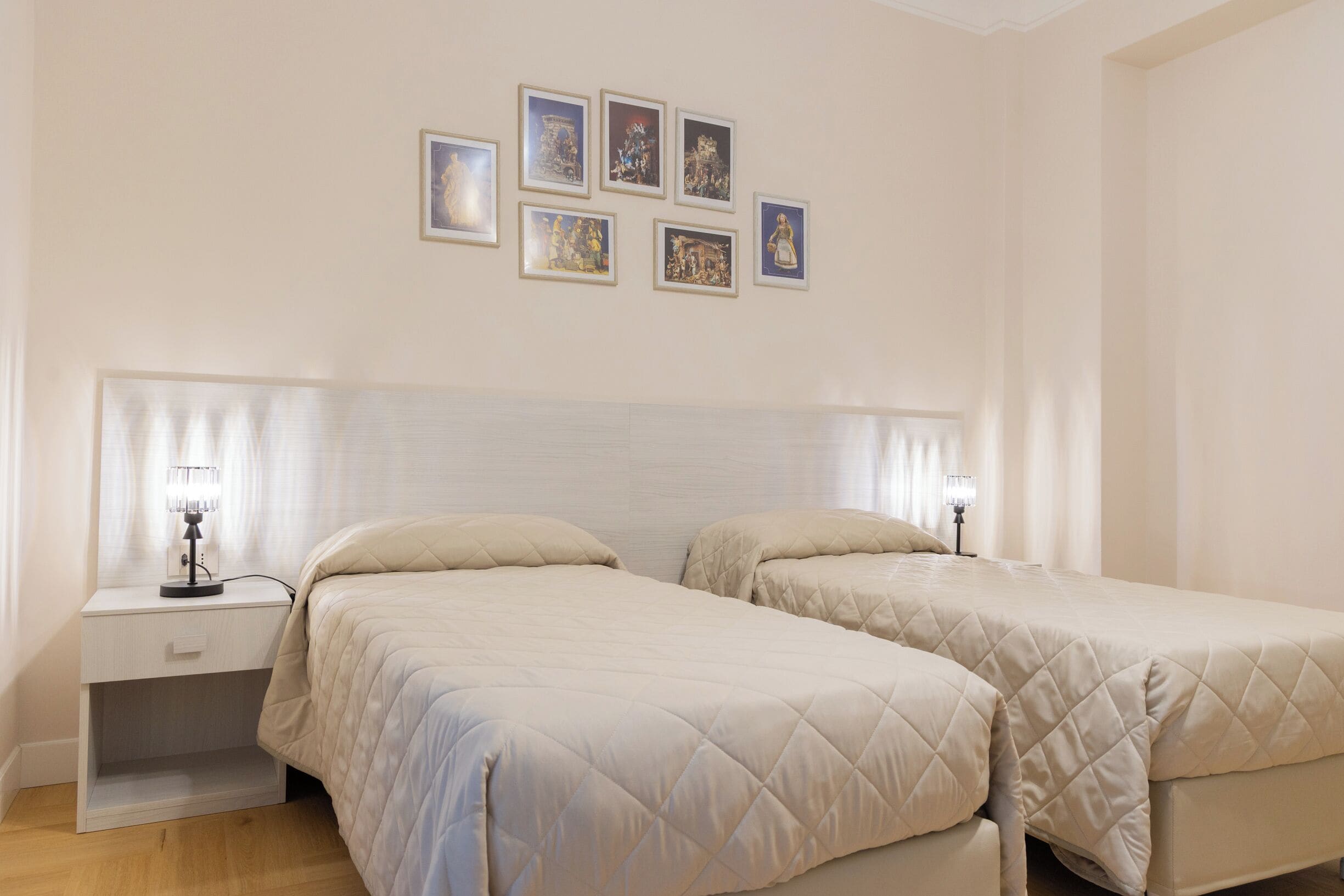A bedroom with two beds, a nightstand, and a wall with six framed pictures.