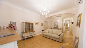 A spacious living room with a wooden herringbone floor, a cream-colored sofa, a wooden chair, and a cabinet with glass doors. - AeP House (Pompei)