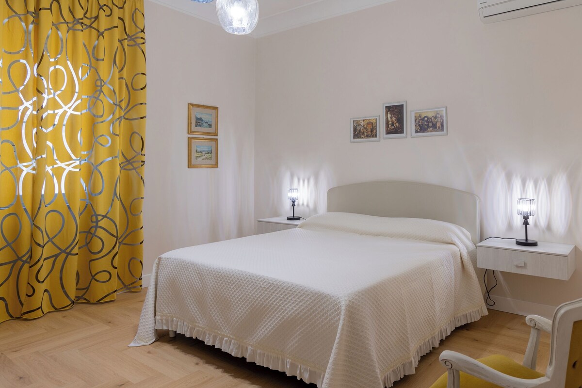 Een slaapkamer met een bed, nachtkastjes, een stoel en een gordijn.