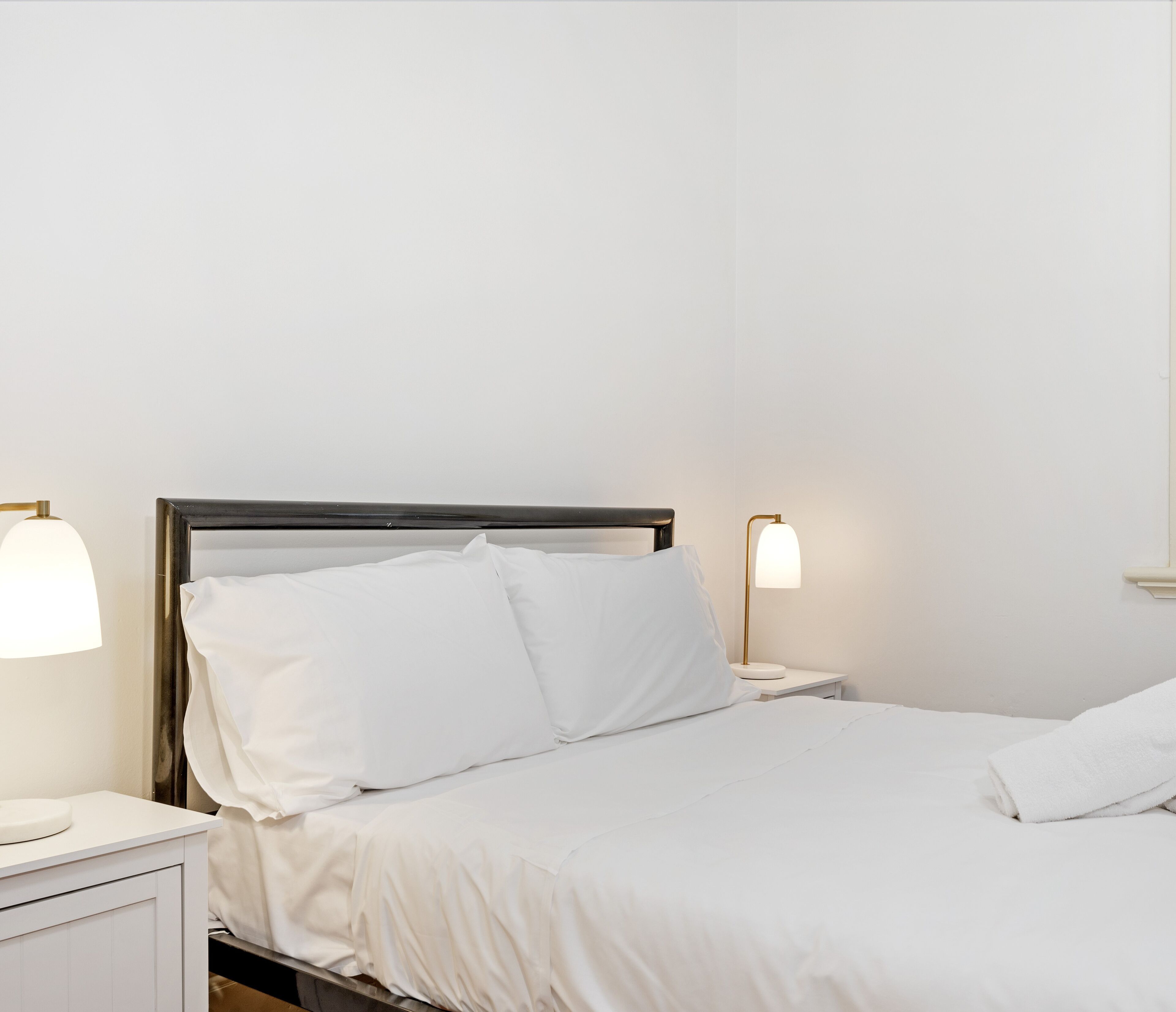 A neatly made bed with white linens and two bedside lamps.