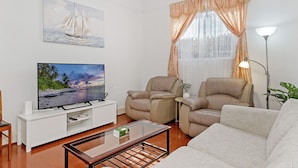 Una sala de estar con televisor de pantalla plana, dos sillones de cuero, un sofá, una mesa de centro y un cuadro de veleros en la pared.