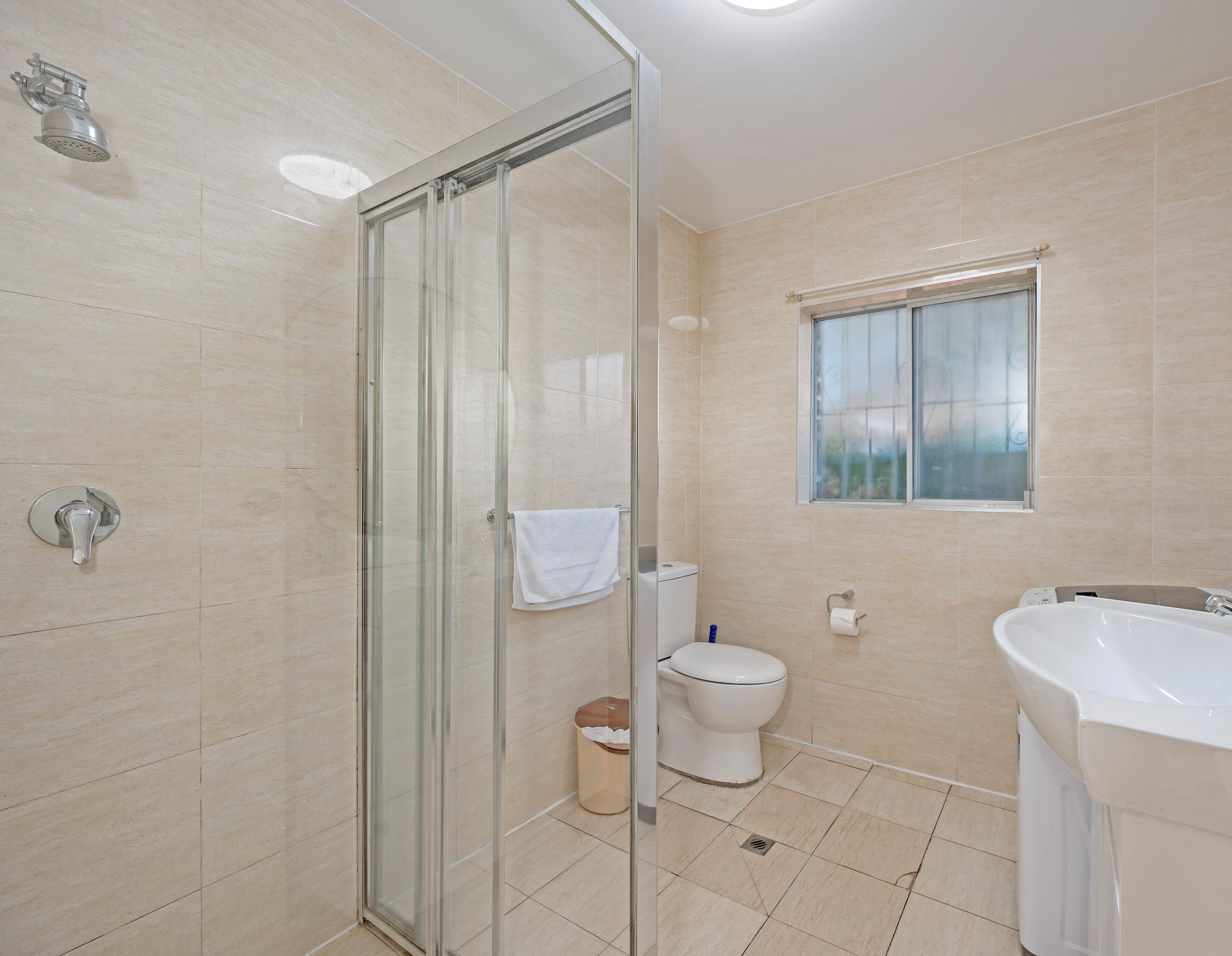 A modern bathroom with a glass shower enclosure, a toilet, a sink, and a window.