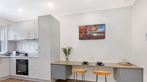Una cocina moderna con horno empotrado, zona de comedor con taburetes y televisor de pared mostrando una imagen panorámica.