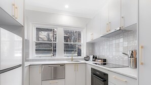 Una cocina moderna con armarios blancos, electrodomésticos de acero inoxidable y un ventanal con vistas a un muro de ladrillo y una obra en construcción.