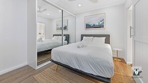 Un dormitorio moderno con una cama grande, un ventilador de techo y una mesita de noche pequeña.