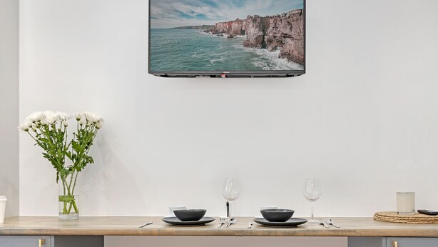 Cocina moderna con vista al mar, dos taburetes de madera, un florero con flores y un comedor.