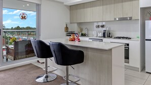 Una cucina moderna con una grande isola, due sgabelli neri, vista sulla città attraverso un'ampia finestra e un balcone con vista sullo skyline.