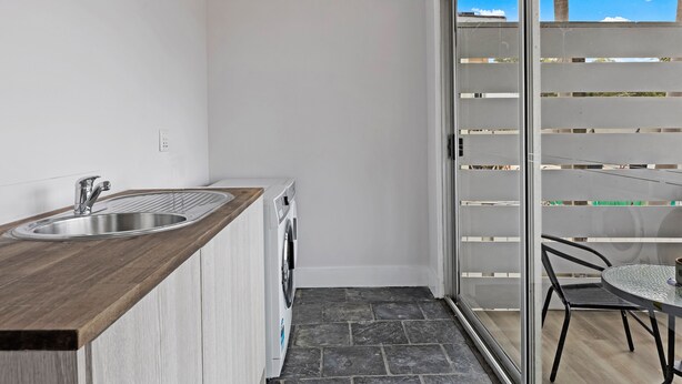 A compact kitchen with a wooden countertop, stainless steel sink, and built-in washing machine. - Kozyguru | Blacktown | Peaceful 3B House (Blacktown)
